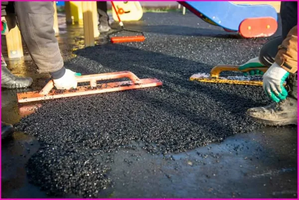 کفپوش درجاریز در رنگ سیاه در حال نصب توسط دو کارگر در محوطه بازی کودکان